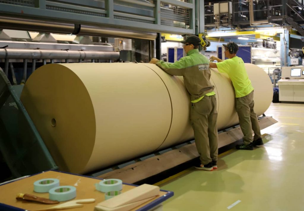 KotkaMills-tehtaan kartonkirulla, jonka vieressä kaksi tehtaan työntekijää.